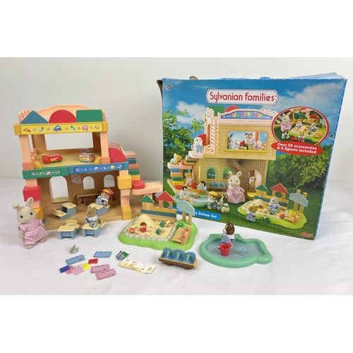 A boxed Flair Toys Sylvanian Families Primrose Nursey Deluxe Set, play building, figures and accessories. Includes 4 animal figures, sandbox and play pieces, water trough, paddling pool, desks & books, hat & shoes. Unboxed approx. 25cm tall.