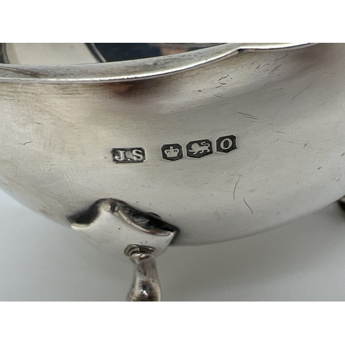 1205 - An Art Deco silver sauce boat with decorative scrolled handle and raised on tripod stepped design ho... 