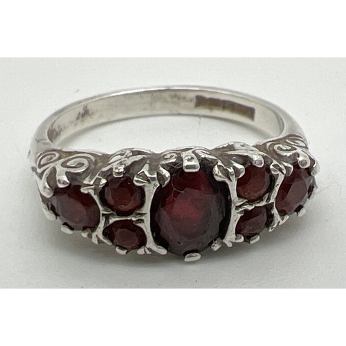 1068 - A vintage silver garnet set dress ring. Central oval cut garnet with 3 round cut garnets to each sho... 