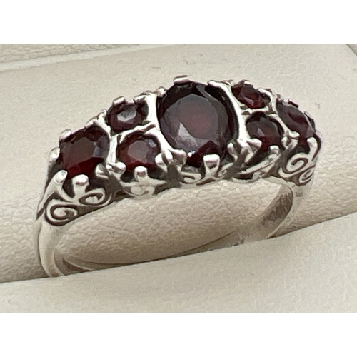 1068 - A vintage silver garnet set dress ring. Central oval cut garnet with 3 round cut garnets to each sho... 