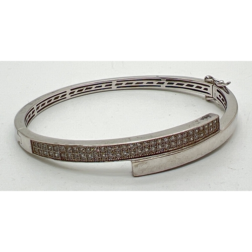 1092 - A silver modern design crossover hinged bangle set with 60 small round cut clear stones. Push clasp ... 