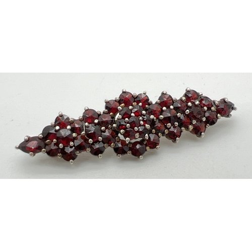 1095 - A silver and garnet cluster brooch set with 38 small round cut stones. Indistinct hallmark on pin of... 