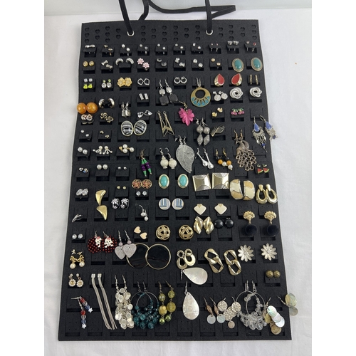 1106 - A black felt hanging earring organiser with over 100 pairs of assorted stud and drop earrings. In va... 