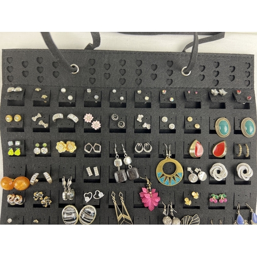 1106 - A black felt hanging earring organiser with over 100 pairs of assorted stud and drop earrings. In va... 