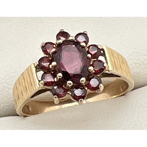 1118 - A vintage 9ct gold and garnet cluster ring with diamond cut detail to shoulders. Large central oval ... 