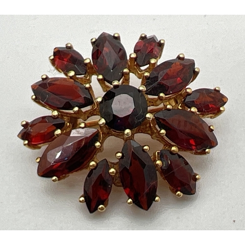 1130 - A small 9ct gold circular flower head design garnet set brooch. A central round cut garnet surrounde... 