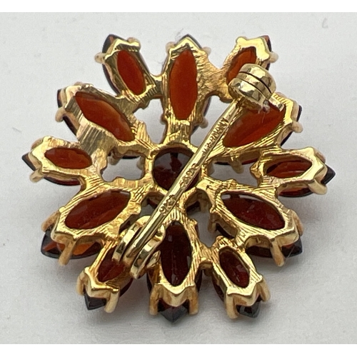 1130 - A small 9ct gold circular flower head design garnet set brooch. A central round cut garnet surrounde... 