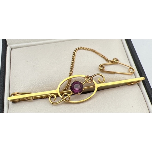 1134 - A 9ct gold bar brooch with twisted scroll detail and central round cut amethyst, complete with safet... 