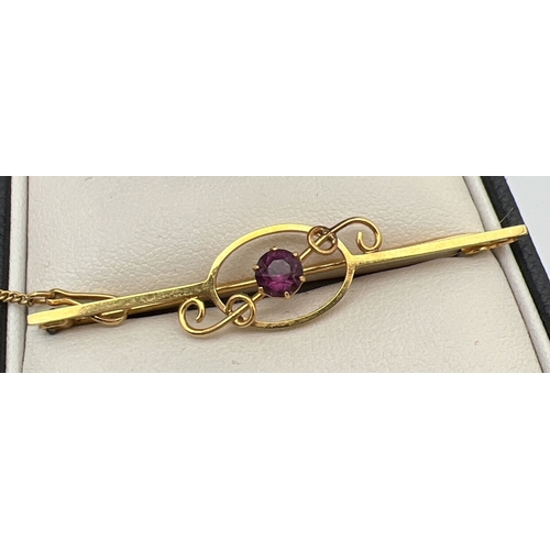 1134 - A 9ct gold bar brooch with twisted scroll detail and central round cut amethyst, complete with safet... 