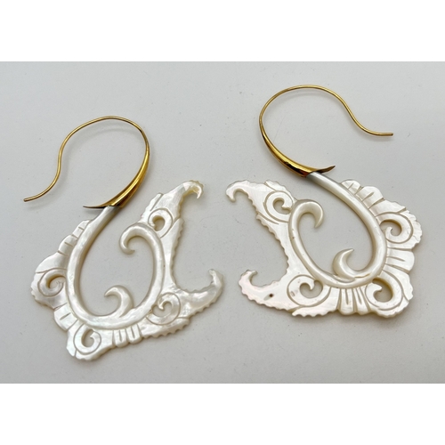 1104 - A pair of oversized decoratively engraved mother of pearl earrings with gold coloured hooked posts. ... 