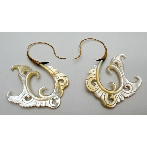 1104 - A pair of oversized decoratively engraved mother of pearl earrings with gold coloured hooked posts. ... 