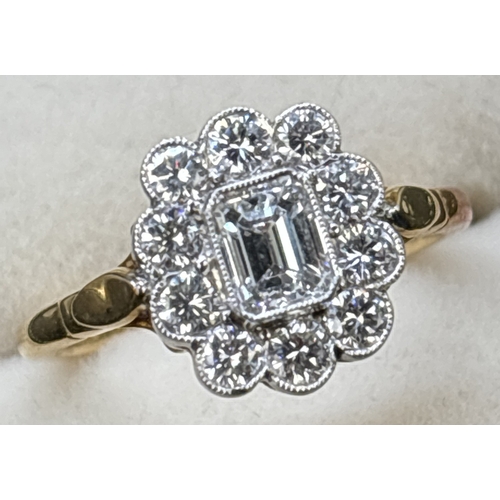 14 - A diamond cluster ring comprised of a central emerald cut diamond with a surround of 10 brilliant cu... 