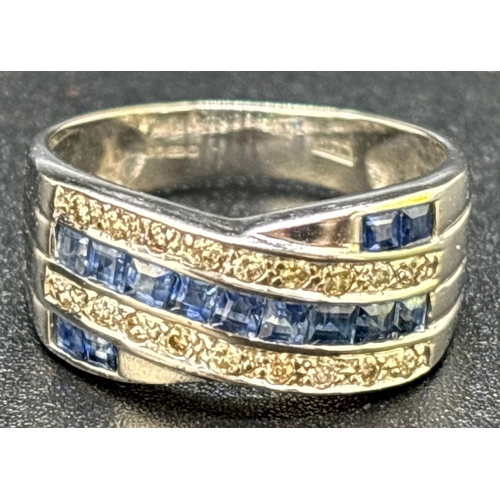 15 - A sapphire and diamond crossover style ring set in 9ct white gold. 13 square cut channel set blue sa... 