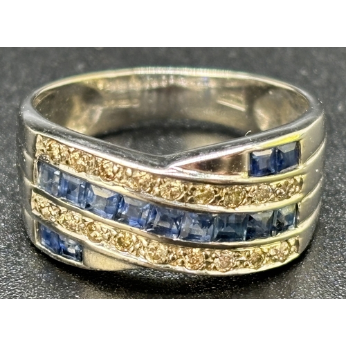 15 - A sapphire and diamond crossover style ring set in 9ct white gold. 13 square cut channel set blue sa... 