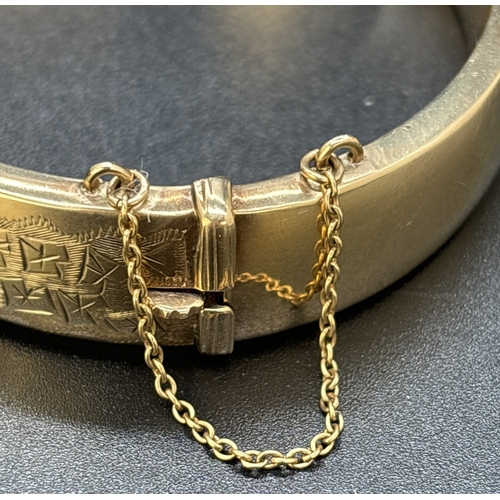 36 - A vintage 9ct gold half engraved hinged bangle with push clasp and safety chain. Engraved fluted edg... 