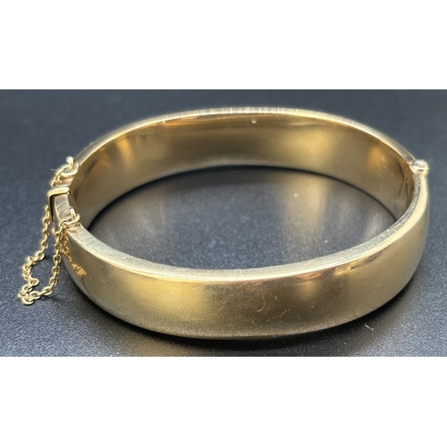 36 - A vintage 9ct gold half engraved hinged bangle with push clasp and safety chain. Engraved fluted edg... 