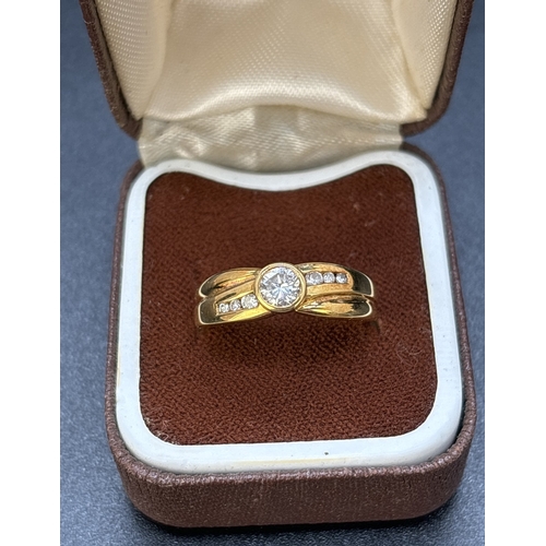 63 - A diamond dress ring set in 18ct yellow gold with crossover design band. Central round cut bezel set... 