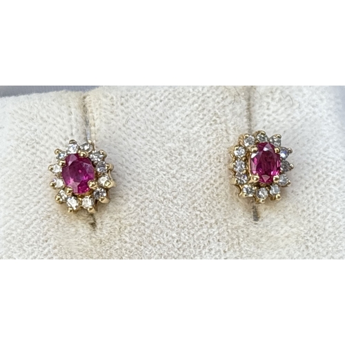 65 - A boxed pair of of ruby and diamond stud earrings. A central oval cut ruby surrounded by 12 round cu... 