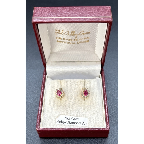 65 - A boxed pair of of ruby and diamond stud earrings. A central oval cut ruby surrounded by 12 round cu... 