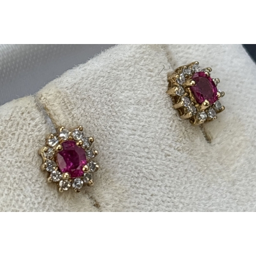 65 - A boxed pair of of ruby and diamond stud earrings. A central oval cut ruby surrounded by 12 round cu... 