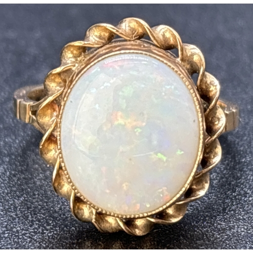 70 - A vintage 9ct gold large oval cut bezel set opal dress ring with twist design surround. Split should... 