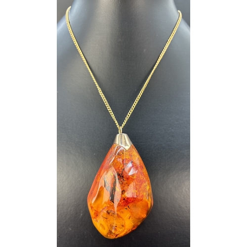 125 - A large natural honey amber pendant with butterscotch and black inclusions, gold cap and bale. On a ... 