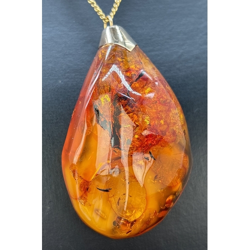 125 - A large natural honey amber pendant with butterscotch and black inclusions, gold cap and bale. On a ... 