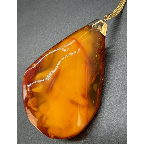 125 - A large natural honey amber pendant with butterscotch and black inclusions, gold cap and bale. On a ... 