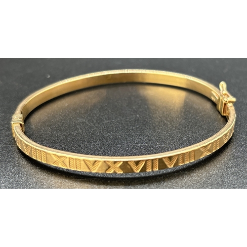 11 - A 9ct gold hinged bangle with Roman numeral decoration, push clasp and safety clip. Gold marks to in... 