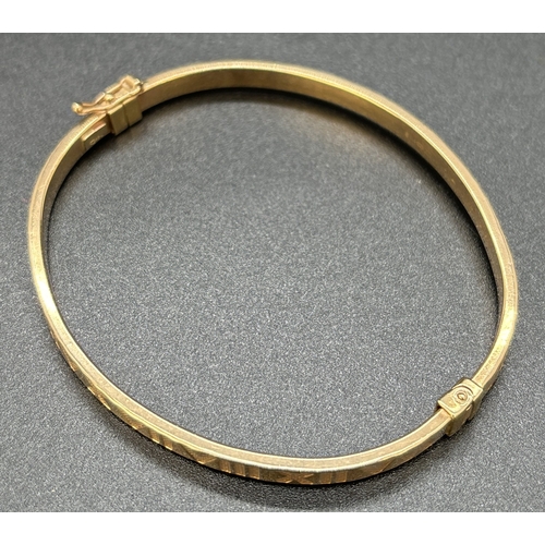 11 - A 9ct gold hinged bangle with Roman numeral decoration, push clasp and safety clip. Gold marks to in... 