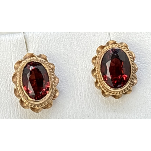 17 - A boxed pair of 9ct gold stud earrings set with oval cut garnets. Rope detail and scallop edge to mo... 