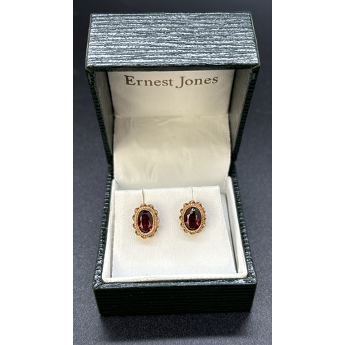 17 - A boxed pair of 9ct gold stud earrings set with oval cut garnets. Rope detail and scallop edge to mo... 