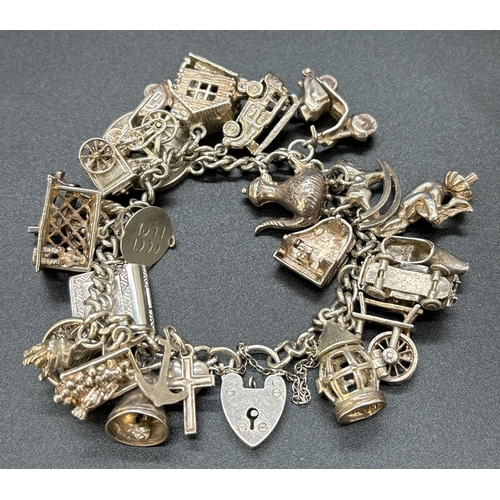 77 - A vintage silver charm bracelet with padlock, safety chain and 23 white metal and silver charms. Man... 