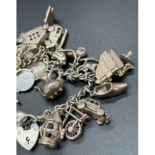 77 - A vintage silver charm bracelet with padlock, safety chain and 23 white metal and silver charms. Man... 