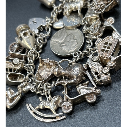 77 - A vintage silver charm bracelet with padlock, safety chain and 23 white metal and silver charms. Man... 