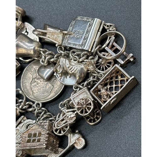 77 - A vintage silver charm bracelet with padlock, safety chain and 23 white metal and silver charms. Man... 