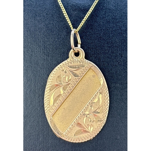 64 - A yellow gold oval shaped flat pendant with floral engraved decoration and brushed gold empty cartou... 