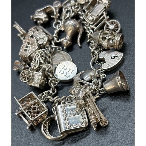 77 - A vintage silver charm bracelet with padlock, safety chain and 23 white metal and silver charms. Man... 