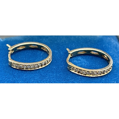 1051 - A pair of 9ct gold diamond set hoop earrings with clip fastening posts. Front of hoops set with smal... 