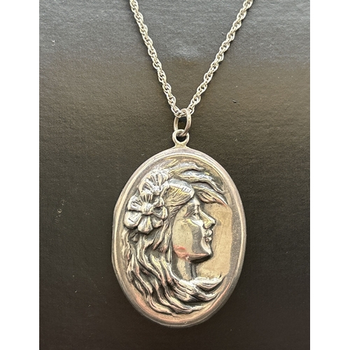 1076 - An oval silver locket with Art Nouveau style embossed maiden's head design on front. On a 24 inch ro... 