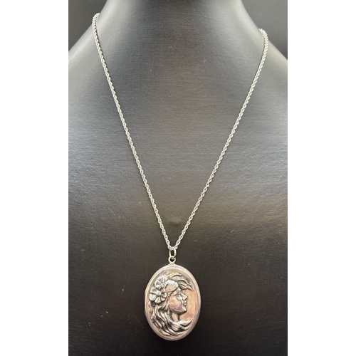 1076 - An oval silver locket with Art Nouveau style embossed maiden's head design on front. On a 24 inch ro... 