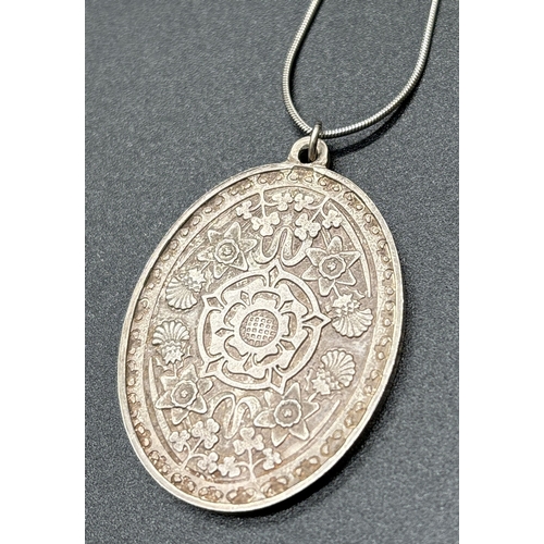 1099 - A large silver oval shaped Queen Elizabeth II 1977 Silver Jubilee pendant decorated with the flowers... 