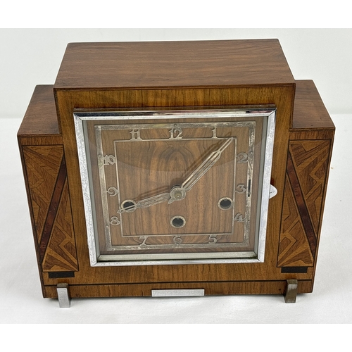 An Art Deco wooden cased westminster chime mantle clock with stepped design and inlaid panels. Pierced white metal hands and overlay face and chrome detail. In working order with lovely deep sounding chimes. With silent feature and handle inside case for holding chime bars. Complete with key and pendulum. Case approx. 22.5(T) x 26cm (W).