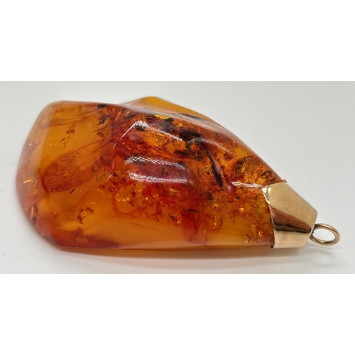 1095 - A large honey amber pendant with natural black and butterscotch inclusions fitted with gold cap and ... 