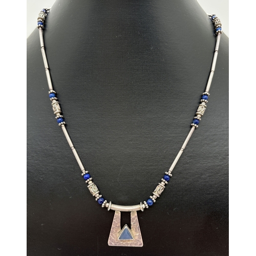 1118 - A silver and lapis lazuli bead fixed pendant necklace. Shaped fixed pedant with hammered effect fini... 