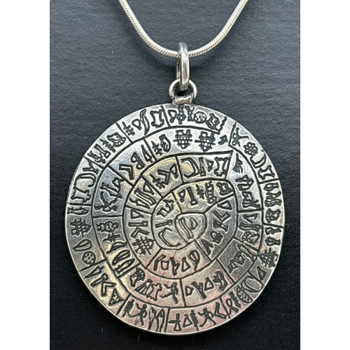 1016 - A silver circular shaped pendant with spiral hieroglyph decoration, on an 18