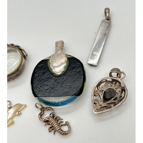 1020 - 6 assorted silver and white metal pendants and charms. A circular foil glass pendant with silver bal... 