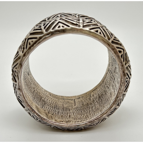 1022 - An unmarked white metal ethnic style bangle with geometric and scroll decoration throughout. Approx.... 