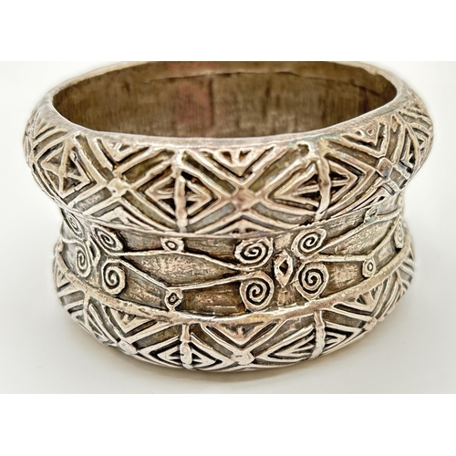 1022 - An unmarked white metal ethnic style bangle with geometric and scroll decoration throughout. Approx.... 