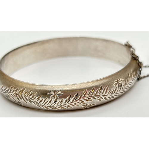 1033 - 2 vintage silver bangles, both with safety chains. A 12mm wide half brushed bangle with fern leaf de... 